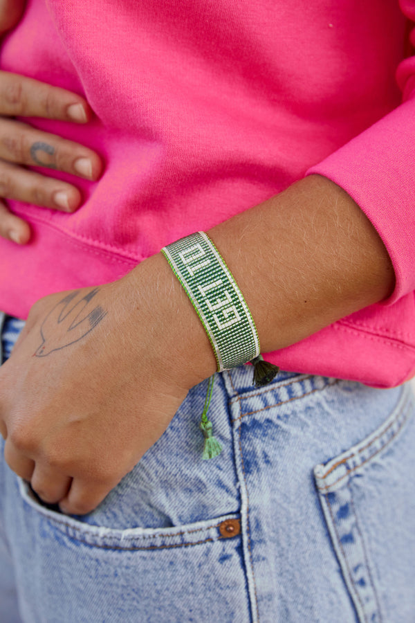 Get To beaded bracelet in sage green with white beads. Model is wearing the bracelet on wrist with a hot pink sweatshirt and denim jeans. Model has a tattoo of a dove on her hand.