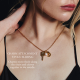 Close-up of a woman wearing a gold chain necklace with a key and crescent moon charm, with text describing the sliding charm attachment style.
