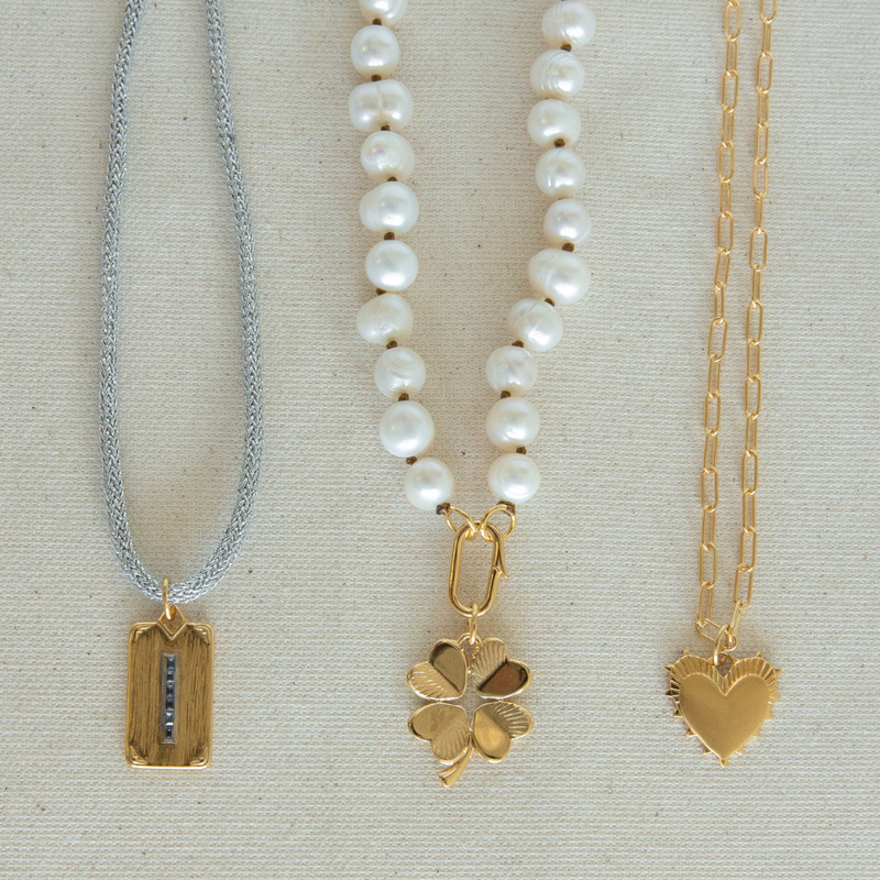 Flat lay image of the Silver Lurex Cord with Carpe Diem Charm, Pearl Necklace with Clover Charm, and Small Heart of Gold Necklace